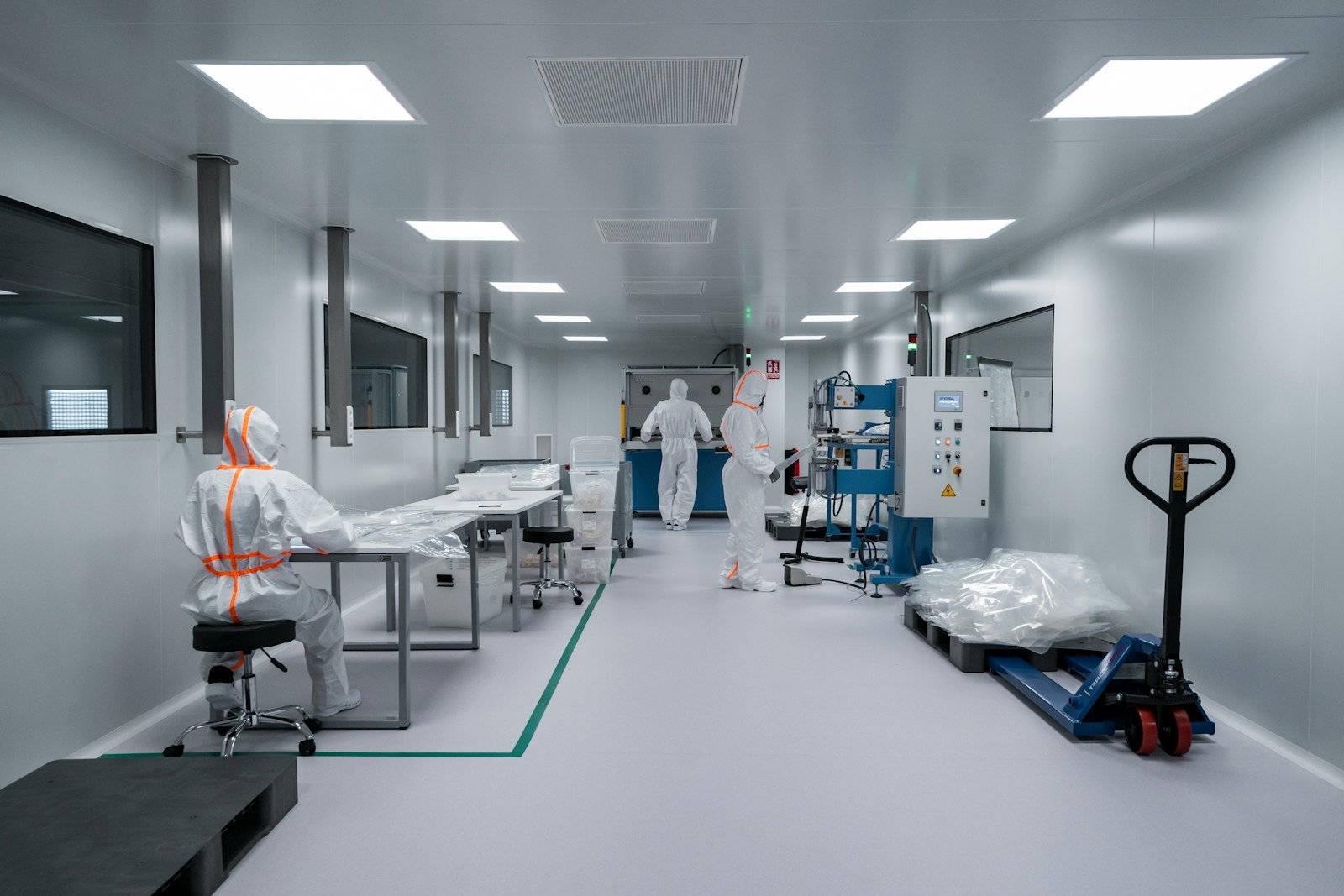 Operators in white cleanroom suits with orange trim working at benches and equipment in a bright medical manufacturing cleanroom