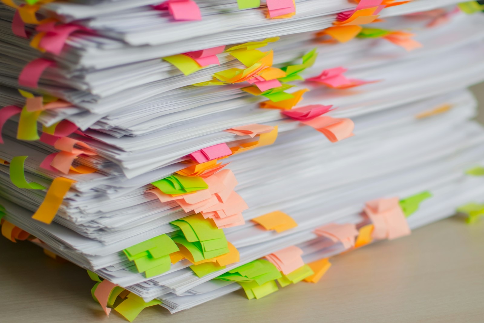 A tall stack of printed documents with pink, orange and green sticky tabs marking pages for revision