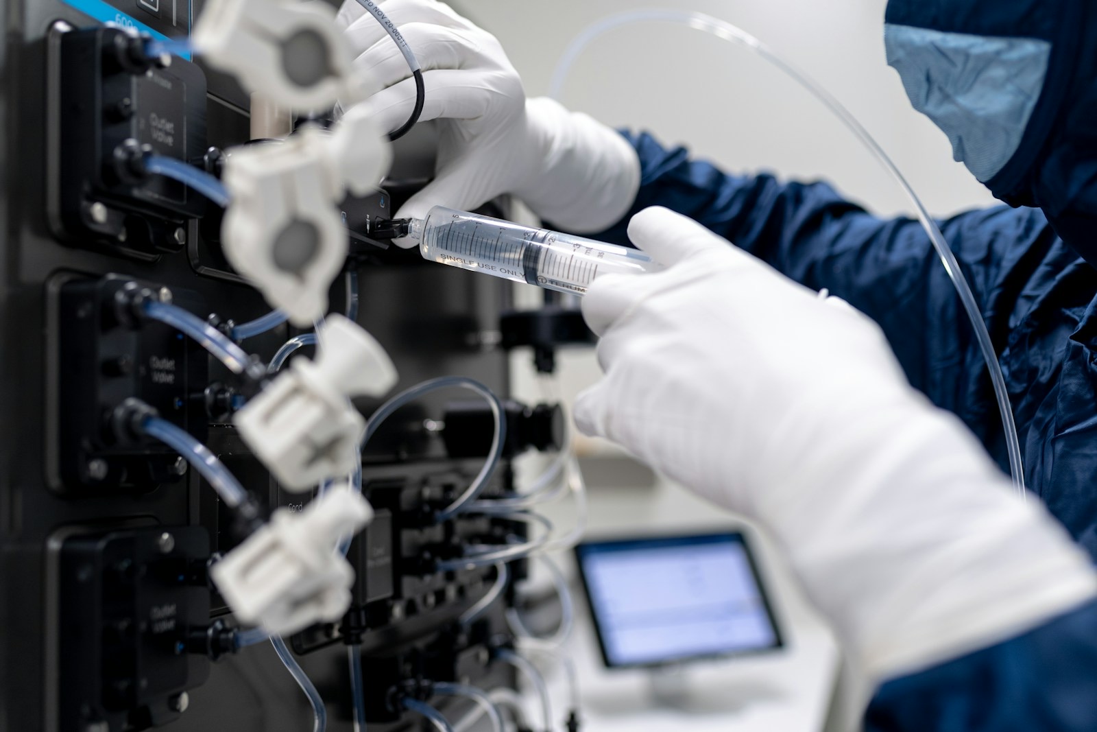 Gloved hands connecting a syringe to the tubing of a laboratory instrument