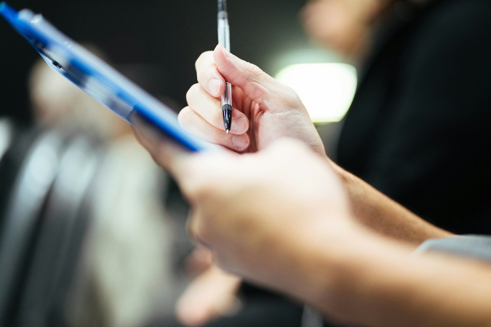 Close-up of a hand holding a pen over a blue clipboard, ready to write